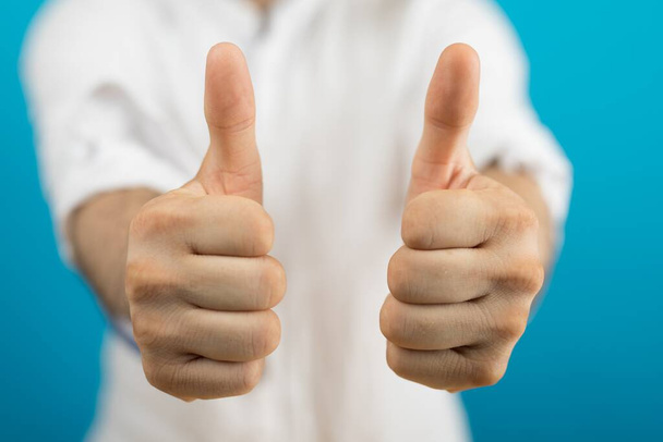 A closeup of a person doing the thumbs-up gesture under the lights on a blurry background - Фото, зображення