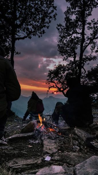 A silhouette of friends sitting in the mountains by the bonfire and enjoying sunset in Munsayari - Foto, Bild