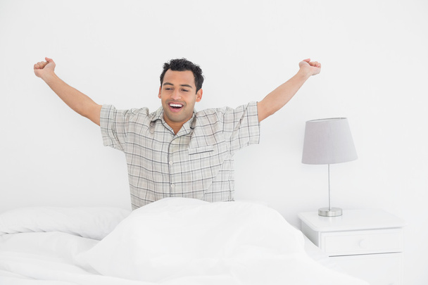 Homem sorridente esticando os braços na cama
 - Foto, Imagem