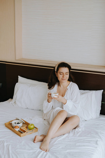 Beautiful woman having breakfast in the hotel on the bed - Фото, изображение