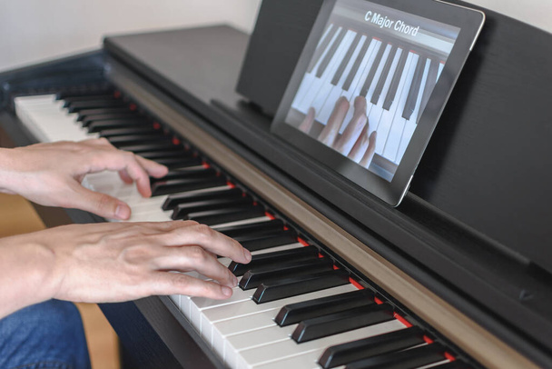 Biały człowiek uczy się grać na pianinie za pomocą lekcji wideo na tablecie. Pojęcie kształcenia na odległość - Zdjęcie, obraz