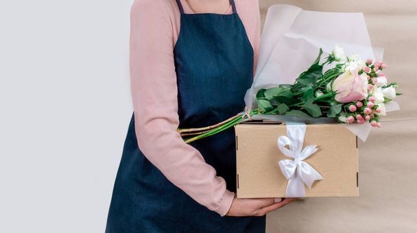 Mitarbeiterin des Lieferdienstes in Uniform verpackt Blumen in Papiertüten und Tüten für Kunden auf weißem und handwerklichem Hintergrund. - Foto, Bild