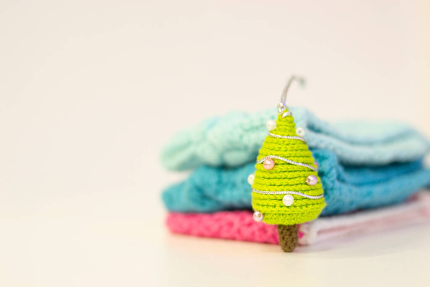 Handmade Christmas knitted gift. Amigurumi toys. Close-up of a Christmas tree knitting with needles on a blurred background. Colorful threads. Copy space. - Foto, imagen