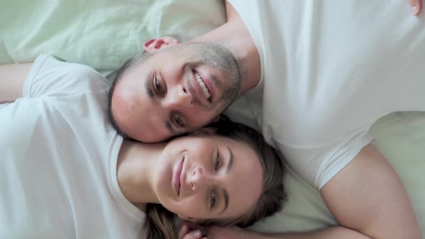 Affectionate young couple lovingly kissing while lying face to face in bed together in the morning - Filmagem, Vídeo