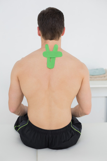 Rear view of a shirtless man with green kinesio tape on back - 写真・画像