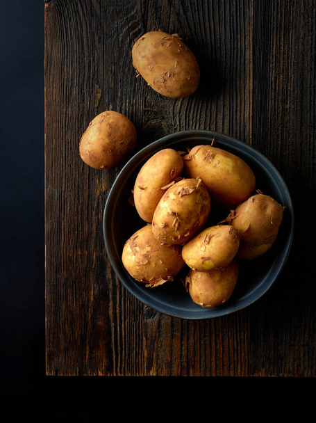 Schüssel mit neuen Kartoffeln auf Holzbrett kochfertig, schwarzer Hintergrund, Draufsicht - Foto, Bild