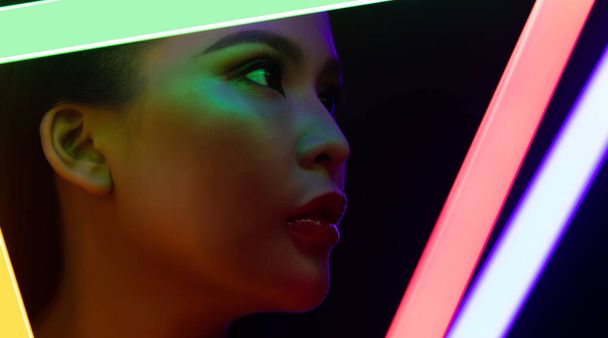 Yüksek Moda Trend Kozmetik Makyajı 'nın Yüzü NEON tüpü ışığı ile kapanıyor, düşük pozlu genç Asyalı kadının tenine etki ediyor, LED çizgisi renginde duygularını ifade ediyor, uzay siyah arka planlarını kopyalıyor - Fotoğraf, Görsel