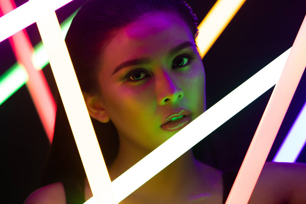 Face Close up of High Fashion Trend Cosmetic make with NEON tube light, effect on skin of young Asian Woman in low explay, expressure by color of LED line, copy space black background - Фото, зображення