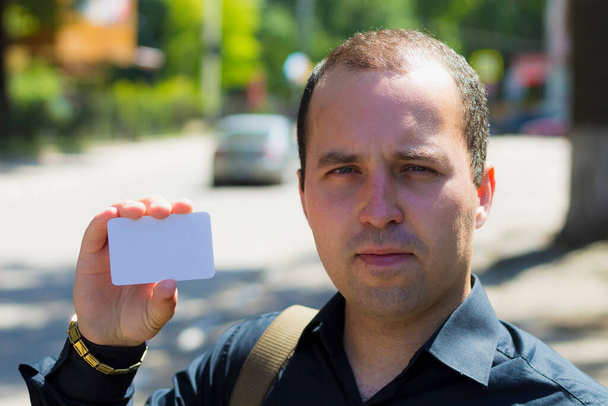 Nuori mies pitää kädessään tyhjää käyntikorttia, jossa on kopiotila kirjoituksen tai tekstin asettamiseksi. - Valokuva, kuva