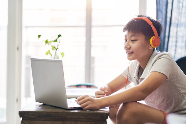 Asiatisches Kind nimmt lächelnd Online-Kurs zu Hause & trägt Headset - Foto, Bild