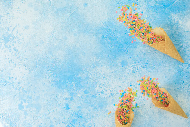 Dulces de confeti brillantes y cono de gofre en azul. Piso tendido, vista superior
 - Foto, imagen
