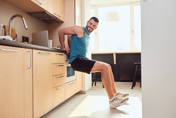 Cheerful young man working out in kitchen - Fotó, kép