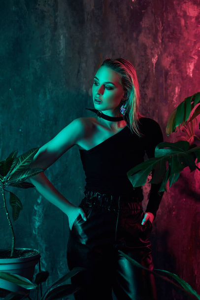 Fashion woman portrait in tropical foliage neon light. Wet hair, perfect figure and makeup. Pink and green neon color. Beautiful girl and monstera leaves - Foto, Imagem