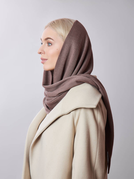 European Muslim woman with a blonde hair in a headscarf shawl dressed on her head. Beautiful girl in coat with soft skin, natural cosmetics - Фото, изображение