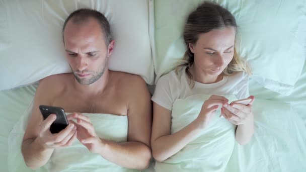 Couple lying in bed using mobile phone while ignoring each other. Man and woman addicted to smartphone social networks technology. - Séquence, vidéo