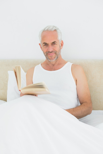 Relaxed mature man reading book in bed - Фото, изображение
