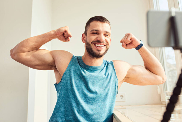 Guapo joven mostrando los músculos del bíceps y sonriendo
 - Foto, imagen