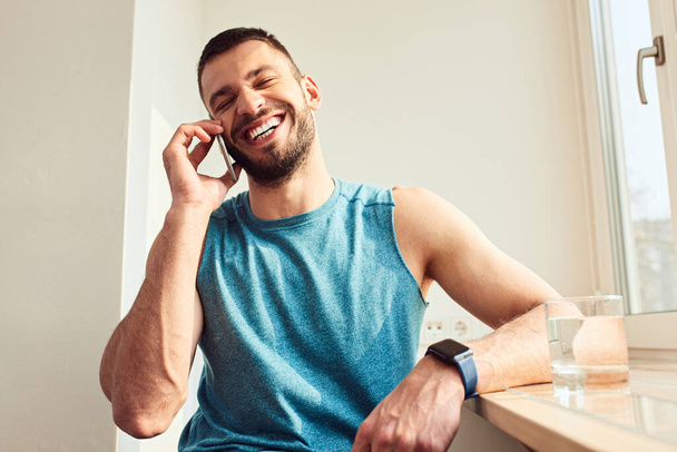 Cheerful young man having phone conversation at home - 写真・画像
