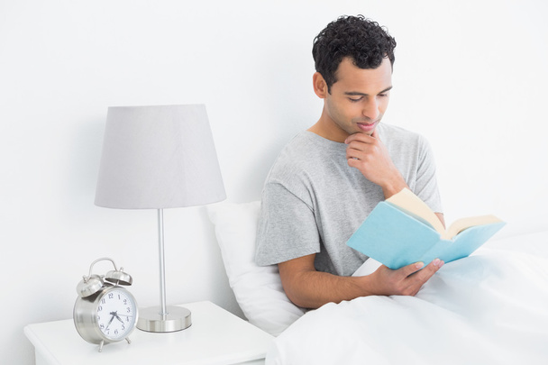 Relaxed man reading book in bed - Photo, image