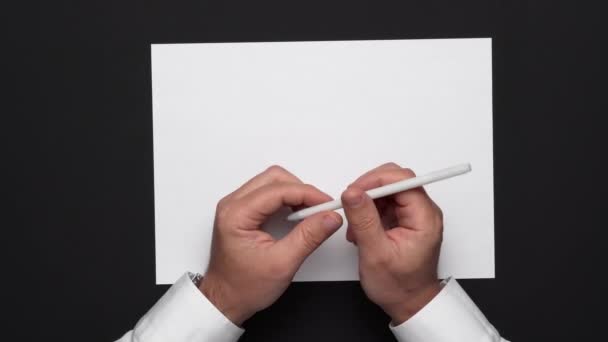 Draufsicht auf ein leeres Blatt Papier und die Hände eines Geschäftsmannes auf einem schwarzen Tisch, weißes Hemd und Armbanduhr - Filmmaterial, Video