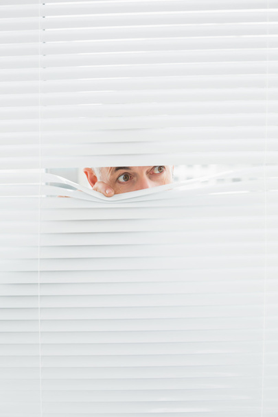 Close-up of a businessman peeking through blinds - Fotoğraf, Görsel