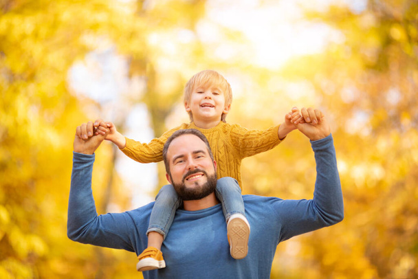 Happy family having fun outdoor in autumn park. Father and son against yellow blurred leaves background - Фото, зображення