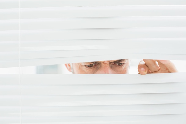 Close-up of a mature businessman peeking through blinds - Fotoğraf, Görsel