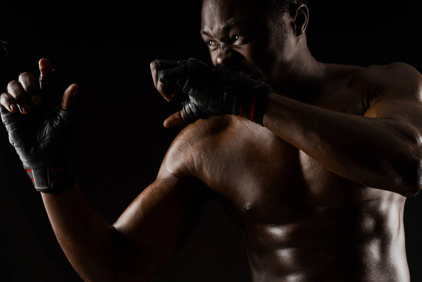 Combattant africain athlétique sur fond noir. Un homme déshabillé à la peau foncée montre un combat. Publicité pour le club sportif et la salle de gym. Boxe professionnelle et karaté
 - Photo, image