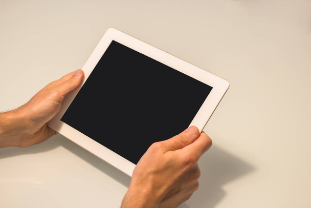 Close up view of man's hands holding tablet with blank black screen and white background - Fotografie, Obrázek