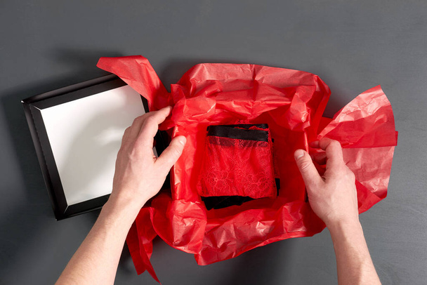 Homme emballage boîte cadeau avec sous-vêtements sexy rouge à la mode sur table en bois gris. Vue rapprochée
. - Photo, image