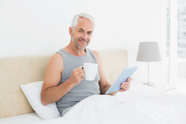 Mature man with digital tablet and coffee table in bed - Foto, immagini