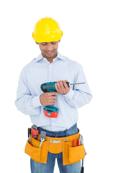 Smiling handsome young handyman looking at drill - Фото, изображение