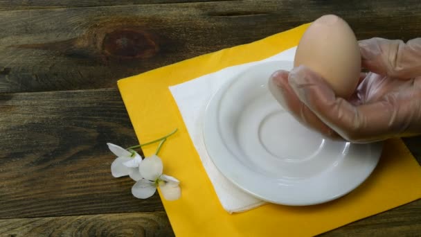 Person nimmt ein gekochtes Ei mit den Händen von der weißen Untertasse, bricht Schale mit Teelöffel und Ei schälen. Nahaufnahme. - Filmmaterial, Video