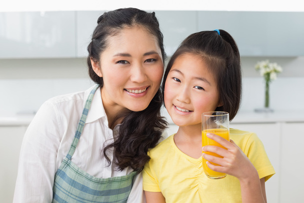 Girl holding orange juice with her mother in kitchen - Fotoğraf, Görsel
