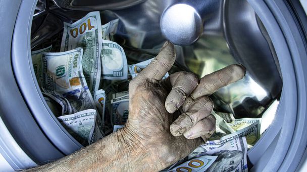Money laundering. Corruption Concealment of taxes. Dollars in the drum of a washing machine and dirty male hand. Concept for social advertising. - 写真・画像