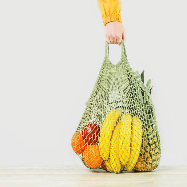 Lieferung von Lebensmitteln. Hand hält Mesh Shoper Tasche mit frischem Obst und Gemüse grünen Produkten. Umweltfreundlicher Lebensstil und Einkaufen. Gesunde Ernährung vegetarisch, Null Abfall-Konzept. Kopierraum. Spende. - Foto, Bild