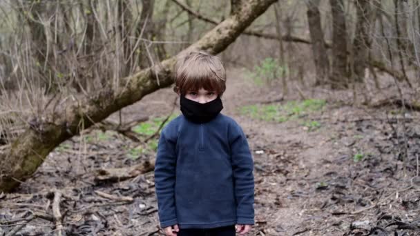 Młody chłopiec w lesie w czarnej masce medycznej wirusa Covid-19 - Materiał filmowy, wideo
