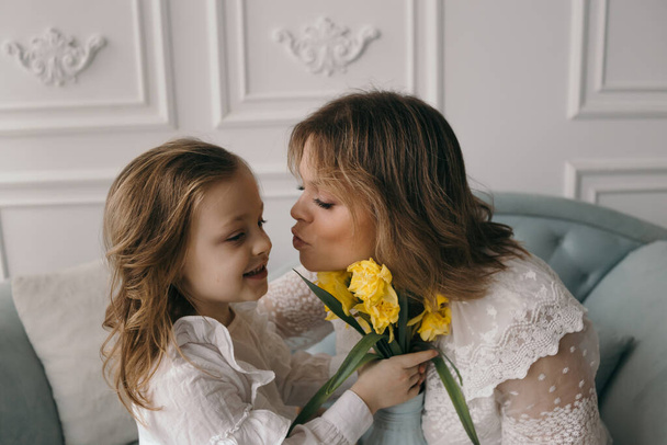 glücklicher Muttertag! Tochter gratuliert Mutter und überreicht Narzisse einen Blumenstrauß und Geschenk - Foto, Bild