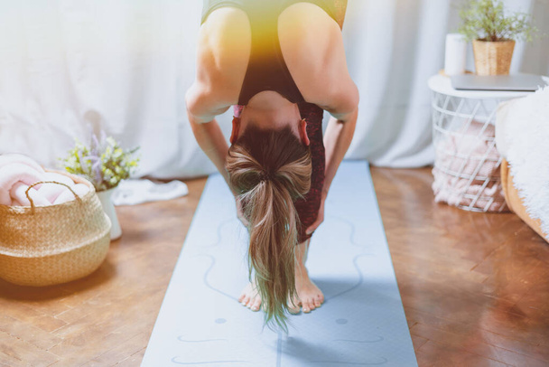 Close up Jonge aantrekkelijke sportieve vrouw die yoga beoefent, voorwaarts buigt, hoofd tot knieën, uttanasana houding, thuis aan het trainen in de woonkamer. Sport en recreatie. - Foto, afbeelding