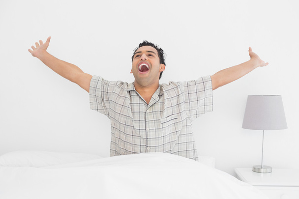 Усміхнений молодий чоловік розтягує руки в ліжку
 - Фото, зображення