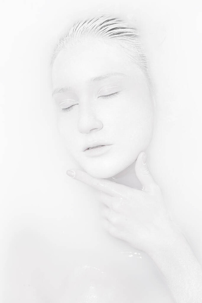 Porträt eines Mädchens mit weißem Gesicht, das in einem Bad mit Milch und Handfläche liegt - Foto, Bild