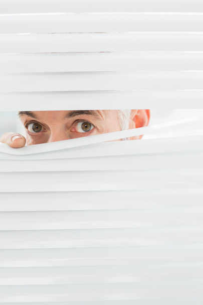 Close-up portrait of a businessman peeking through blinds - Fotoğraf, Görsel