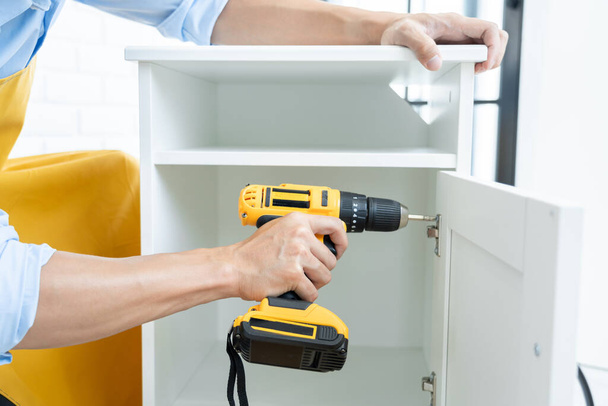 Close up portrait and details of caucasian male worker using electric screwdriver instrument in hand and repairing new wooden desk, home improvement concept - Photo, Image