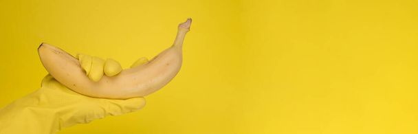 Γυναικεία Χέρι με χρωματιστά λαστιχένια γάντια που κρατούν μπανάνα στο φόντο  - Φωτογραφία, εικόνα