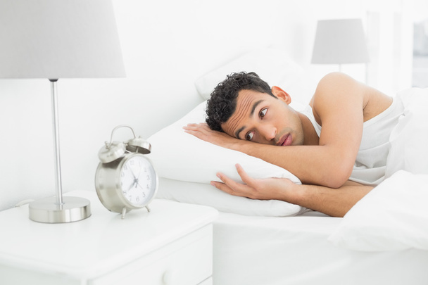 Sleepy man looking at the alarm clock in bed - 写真・画像