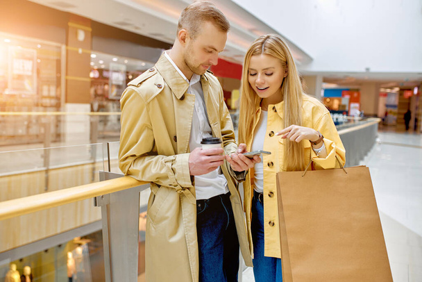 stylish couple use smartphone in aisle of shopping mall - Fotó, kép