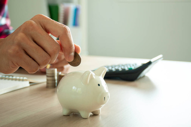 Geschäftsmann mit Münzen in einem Sparschwein mit Taschenrechner und einem Stapel Münzen. Konzept spart Geld für Finanzbuchhaltung - Foto, Bild