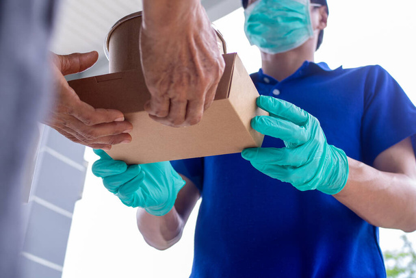 The shipper wears a mask and gloves, delivering food to the home of the online buyer. stay at home reduce the spread of the covid-19 virus. The sender has a service to deliver products or food quickly - Fotografie, Obrázek