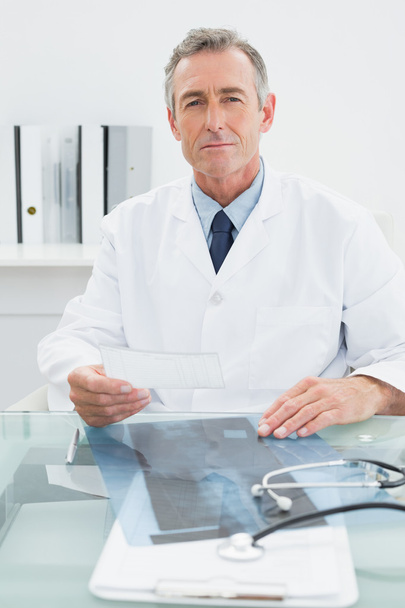 Male doctor reading a note at desk in office - Photo, Image