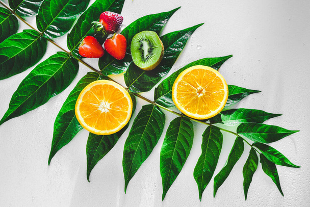 slices of orange, kiwi, strawberries on a green branch on a white background. macro. Healthy fruits. Healthy food - Фото, зображення